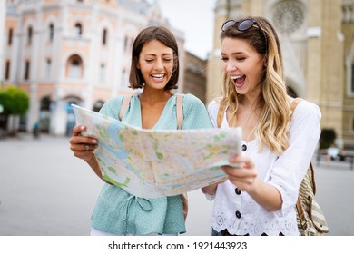Holidays, travel, friends and tourism concept. Beautiful girls looking into tourist map in the city