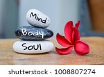 Holistic health concept of zen stones with deep red plumeria flower on blurred background. Text body mind soul.