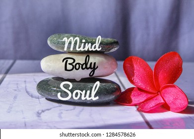 Holistic Health Concept Of Zen Stones With Deep Red Plumeria Flower On Blurred Background. Text Body Mind Soul.