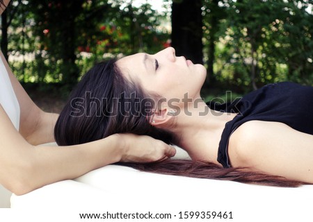 holistic therapist performs Cranial sacral therapy to a young woman - girl receives outdoor shiatsu treatments
