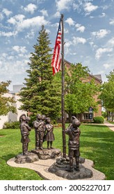 Holland, MI, USA - June 8, 2008: Closeup Of Pledge Of Allegiance Group Of 5 Statues Of Children In Brown Bronze Against Green Foliage Under Blue Cloudscape. American Flag.