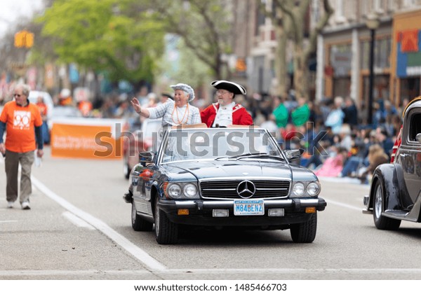 Holland, Michigan, USA - May 11, 2019: Tulip Time\
Parade, Man and woman wearing traditional dutch clothing riding on\
a Mercedez during the\
parade