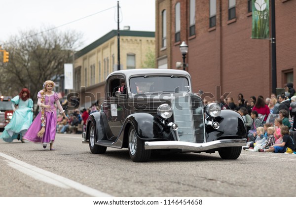 Holland, Michigan, USA - May 12, 2018 Members of\
Everafter West Michigan dress up as disney princess  with a classic\
car on the foreground, at the Muziek Parade, during the Tulip Time\
Festival