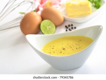 Hollandaise sauce with black pepper and the ingredients (butter, egg, lemon) of the sauce in the back (Selective Focus, Focus in the middle of the bowl)
