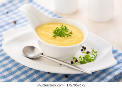 Hollandaise sauce. Classic French cuisine sauce. Emulsion sauce of butter and egg yolks with vinegar. Served in a gravy boat on a blue napkin. Close-up.