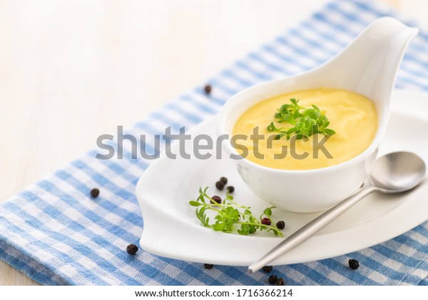 Hollandaise sauce. Classic French cuisine\
sauce. Emulsion sauce of butter and egg yolks with vinegar. Served\
in a gravy boat on a blue napkin.\
Close-up.\
