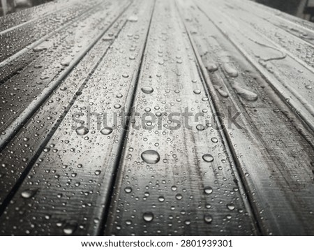 hollow structural steel sections (rectangular or square steel tubes) .The surface is covered in beads of water or condensation, showing high surface tension (often seen on clean metal, lightly oiled surfaces, or materials left outdoors in the rain).