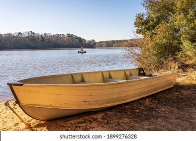 Holly Springs, North Carolina USA-01 19 2021: A Small Aluminum Boat Beached on the Shore of Bass Lake in Winter.