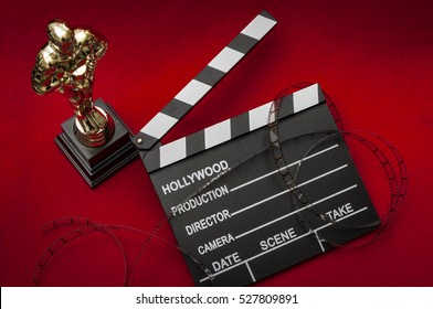 Hollywood Film Awards Concept With Shiny Metallic Movie Award Wrapped In Celluloid Film Strip On Red Carpet With Clapper Board