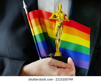 Hollywood Golden Oscar Academy award statue with lgbt flag in hand. Success and victory concept.