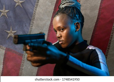 Hollywood movie style portrait of young attractive and confident black African American woman holding gun as special federal agent isolated in USA flag background pointing the handgun