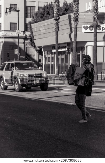 HOLLYWOOD, UNITED STATES\
- Nov 22, 2021: A grayscale shot of homeless crossing the street\
carrying a heavy box