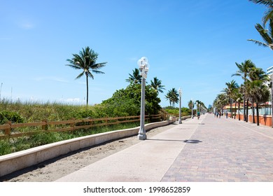 Hollywood, USA - May 6, 2018: Beach Broadwalk Board Walk In Florida Miami With Sunny Day And People Walking On Promenade By Restaurants And Palm Trees