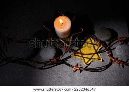 Holocaust memory day. Barbed wire, stones, yellow star and burning candle on black background