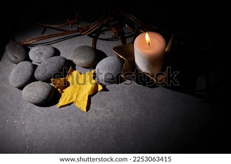 Holocaust memory day. Barbed wire, stones, yellow star and burning candle on black background