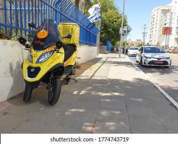 HOLON, ISRAEL. July 12, 2020. Yellow Israel Magen David Adom First Aid Paramedic Scooter Bike And A Police Car Parked On The Side Of The Road. Israel Emergency Services Concept Image.