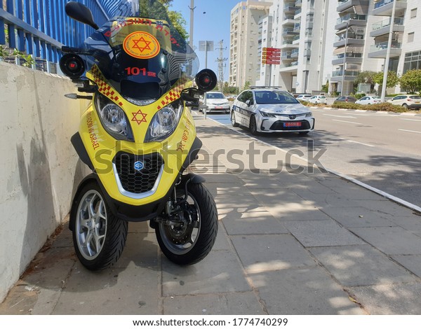 HOLON,\
ISRAEL. July 12, 2020. Yellow Israel Magen David Adom First Aid\
paramedic scooter bike and a police car parked on the side of the\
road. Israel emergency services concept\
image.