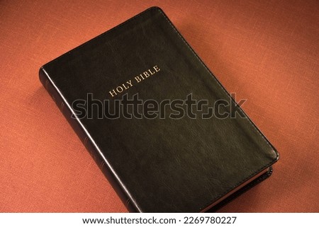 Holy Bible, black cover, brown background. Gold letters.