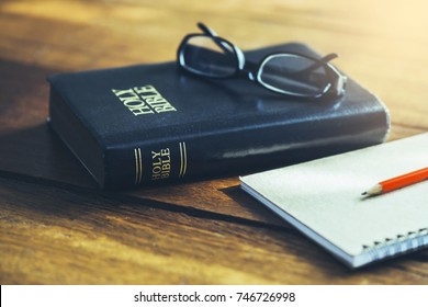  holy bible with eye glasses and note book, pencil   on wooden table with window light in the morning, copy space