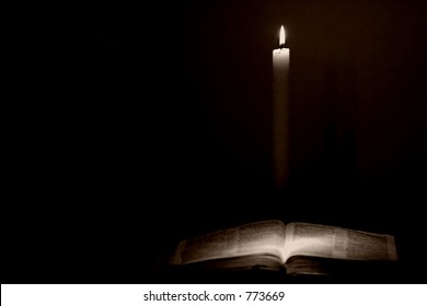 Holy Bible lit by candle light in a vintage style.