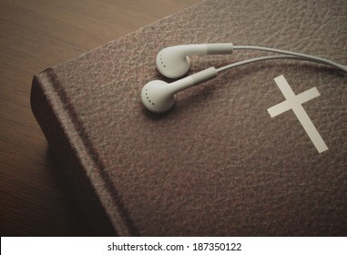 Holy Bible With A Resting Pair Of Earbuds Over It. The Word Of God Through Hearing.