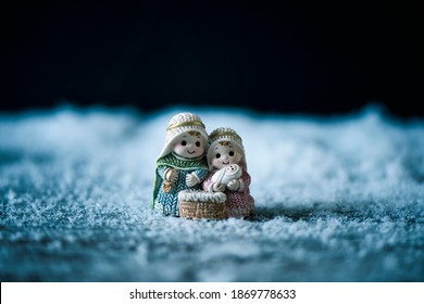 The Holy Family, The Child Jesus, The Virgin Mary And Saint Joseph, On The Snow Against A Black Background With Some Blank Space On Top