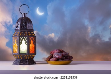 Holy month of Ramadan concept. Righteous Muslim Lifestyle. Fasting. Ramadan lantern (Fanous), dates.. Sunset clouds with a crescent moon on the background. Space for text on the right. - Powered by Shutterstock