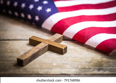 A holy wooden Christian cross laying on a wood background with an American flag.