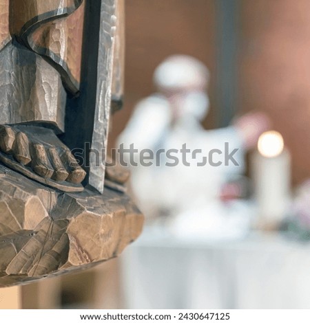 Holy wooden statue. Carved wooden feet, detail of wooden statue of a Saint. In the blurred background a priest celebrates Mass.