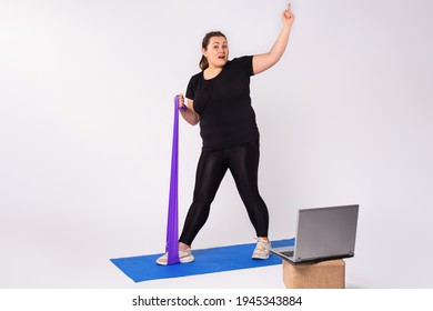 Home Activity And Training, Online Fitness Class. Overweight Blonde Woman Doing Stretching Exercises, Violet Resistance Band Watching Video Guide, Blue Fitness Mat, Using Laptop, White Background