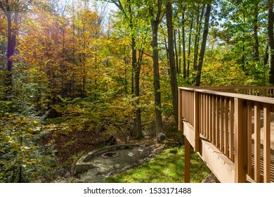 Home In The Autumn Woods Showing Fall Foliage, Section Of A Large Deck, And A Fire Pit.  Outdoor Living Concept.