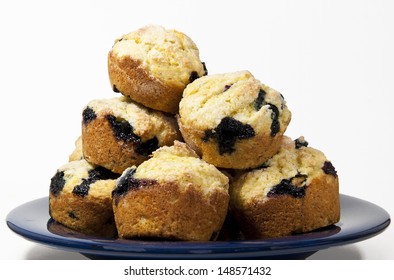 Home Baked Blueberry Corn Muffins Piled On A Blue Glass Plate Against A White Background