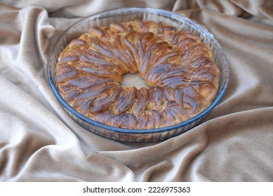 Home baked bread cake with kaki and cheese filling. Sweet bread roll sliced and braided in wreath in glass baking pan. Advent bread, wreath with fresh cheese and kaki fill on beige velvet. - Shutterstock ID 2226975363