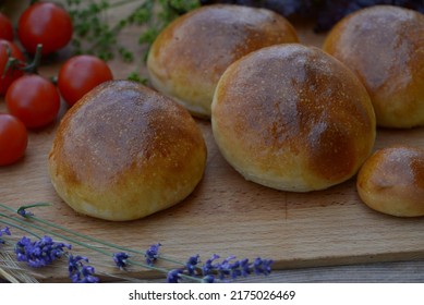 Home baked burger buns, small breads with shiny crust on wooden board. Delicious sandwich breads with cherry tomatoes and lavender flowers. Fresh baked bread rolls with soft crust and fluffy crumb.  - Shutterstock ID 2175026469