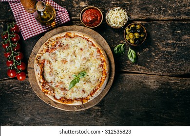 Home Baked Margarita Pizza With Fresh Ingredients Including Tomatoes, Mozzarella Cheese, Olives , Basil And Oil On A Rustic Wooden Kitchen Counter, Viewed From Above