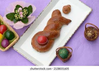 Home Baked Sweet Bread Bunny Holding Red Coloured Egg. Easter Cake With Walnut Stuffing In A Shape Of Easter Rabbit With Easter Eggs. Chocolate Roll Stuffed With Walnuts And Braided In Bunny Shape.