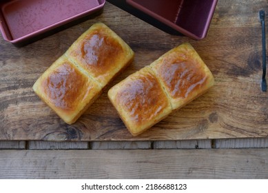 Home Baked Sweet Bread Rolls On Wooden Board. Bread Texture Of Sweet Buns For Sweet Sandwich With Baking Pans In Background. Delicious Small Breads With Shiny Crust And Soft Crumb.