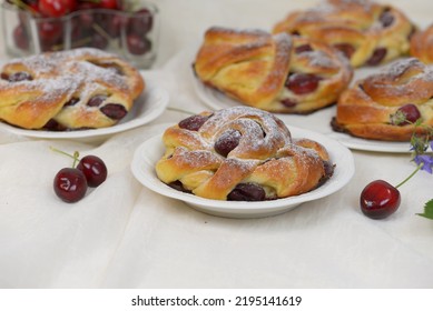 Home Baked Sweet Bread Rolls With Cherries On White Tablecloth. Small Fruit Cakes, Home Baked Milk Buns With Cherries On White Plate With Glass Bowl Of Fresh Cherries In Background.