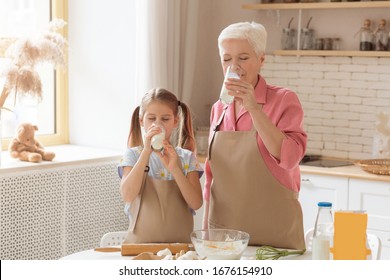 Home Baking. Older Woman And Her Granddaughter Drinking Milk While Cooking In Kitchen, Copy Space