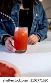 The Home Bartender Serves A Red Color Cocktail With A Metal Pipe. A Cut Grapefruit In The Foreground. The Bartender In A Denim Jacket.