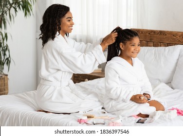 Home Beauty Salon. Loving Black Mom Braiding Hair To Her Cute Little Daughter, Having Domestic Spa Day, Wearing Bathrobes While Relaxing Together On Bed, Having Fun And Enjoying Time With Each Other - Powered by Shutterstock