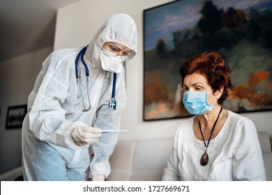 Home care doctor wearing personal protective equipment(PPE).Infection and cross-contamination during home visit to suspect COVID-19 senior patient.Checking temperature with termomether.Fever symptoms