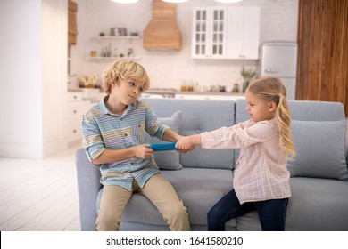 At home. Children fighting, taking tablet from each other and feeling aggressive - Powered by Shutterstock