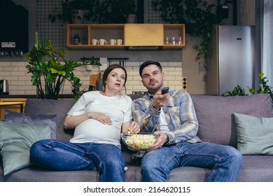 Home cinema. Young family. Pregnant woman and man sitting on sofa at home, watching TV, movie, eating popcorn. Have a good time together - Powered by Shutterstock