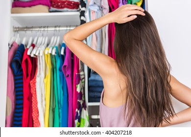 Home closet indecision woman choosing her fashion outfit on clothing rack. Shopping spring cleaning concept. Morning woman having too many clothes thinking of what to wear in organized clean walk-in.