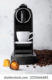 Home coffee machine with white cup and pods capsules on light kitchen background with raw aroma beans