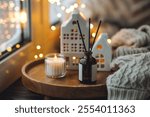 Home comfort, coziness, aromatherapy. Cozy interior with knitting, burning scented candles and aroma perfume diffuser in the living room. Christmas holiday spirit, atmospheric decor for festive mood