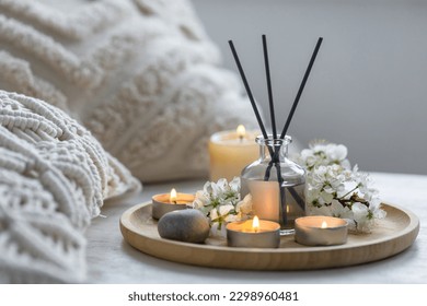 Home comfort, coziness, aromatherapy. Cozy interior with knitting, burning candles and aroma perfume diffuser in the living room. Fresh spring blossom fragrance, apple cherry flowers.