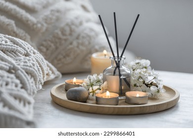 Home comfort, coziness, aromatherapy. Cozy interior with knitting, burning candles and aroma perfume diffuser in the living room. Fresh spring organic blossom fragrance, apple cherry flowers.