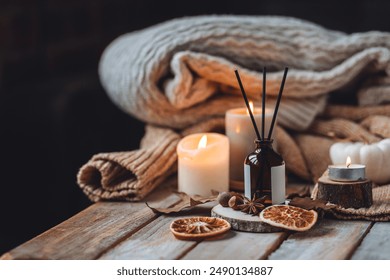 Home comfort, coziness, aromatherapy. Cozy interior with knitting, burning candles and aroma perfume diffuser in the living room. Fall scent, sweet pumpkin pie fragrance, dry leaves, autumn mood